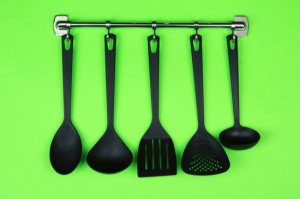 Black kitchen utensils on silver hooks, on green background